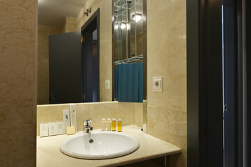 Small bathroom with cream marble tiles, white fixtures, round sink and frameless wall mounted mirror