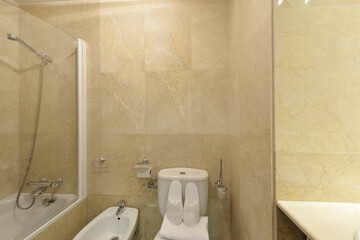 Bathroom with cream marble tiles, white toilets and shower cabin with glass partition