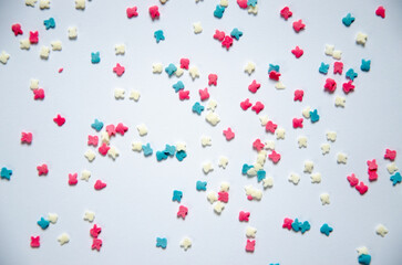 On a white sugar backing lies a sweet pastry topping in the form of pink hearts, orange, turquoise and red peas, and green, blue and yellow sticks