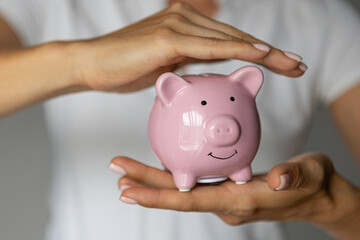 female hands puts a coin in a pink piggy bank. The concept of saving money or savings, investment
