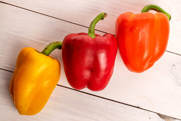Three whole organic fresh juicy tasty bell peppers, close-up, on a painted white table top made of wood, top view.