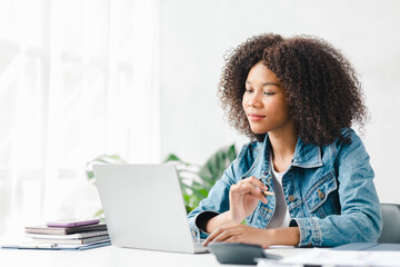 American teenage woman sitting in white office with laptop, she is a student studying online with...