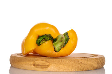 Two halves of bright yellow, organic ripe juicy bell pepper, on a round bamboo tray, close-up, on a white background.