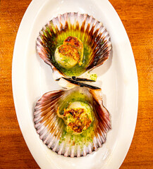 Pintxo of grilled scallops on the grill, seasoned with parsley oil and served in their own shells....