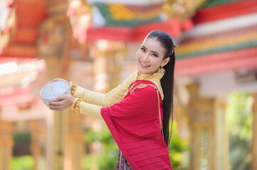 A beautiful Thai woman in Thai dress with gold ornaments holds a cup of water for Songkran Festival or Thai New Year