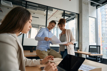 Obraz premium Woman sits at laptop, while her colleagues discuss documents