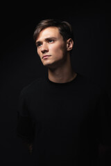 Fototapeta premium A guy of model appearance in black clothes poses on a black studio background. Male fashion portrait