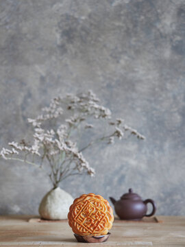 Mid-autumn festival composition, front view of moon cake on a table, teapot and vase with dried flowers on gray background with copy space.