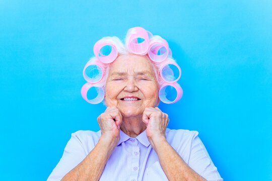 Charming old woman with curlers on white grey hair wear shirt getting ready for date isolated on brigth blue background