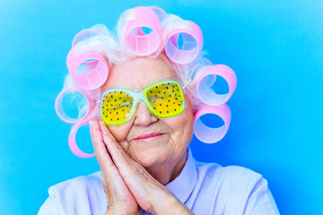 cute 80 years old woman with curlers on white hair wear hyaluronic acid eyes mask with in blue...