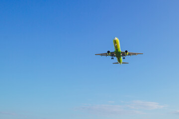 Fototapeta na wymiar Passenger plane of yellow-green color flies in the blue sky, air transportation concept, population evacuation