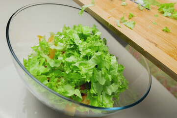 salad with greens, tomatoes and radishes in a glass bowl. sliced lettuce on a board with a knife, top view