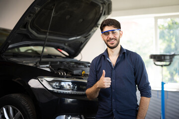 Happy technician bearded brunet mechanic man 20s in safety glasses work in vehicle repair shop show...