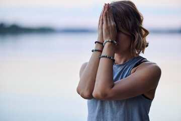 A fit yogi woman is standing near the river in nature and doing sun salutation in the morning.