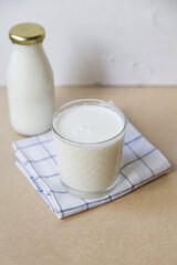 A glass of ayran on a light brown background, a bottle of ayran next to it