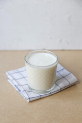 A glass of ayran on a light brown background, behind a white wall