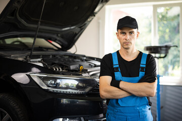 Portrait of a car mechanic crosses hands in a car workshop in blue uniform with equipment looking...