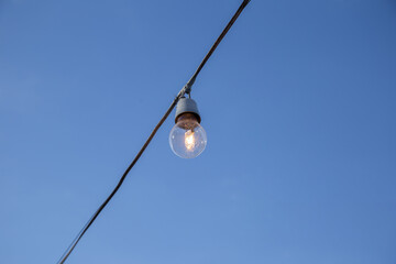 Uma lâmpada conectada a um fio elétrico com céu azul ao fundo.