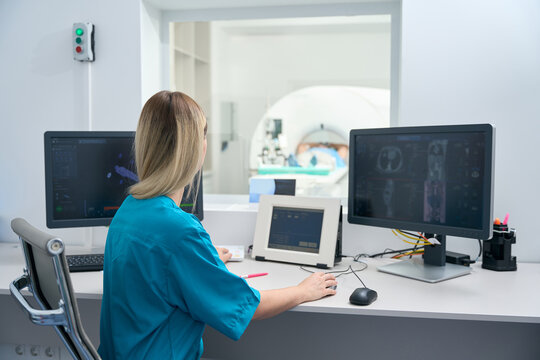 Woman in medical clothes sits at table in tomography room