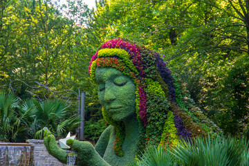 a stunning summer landscape in the garden with The Earth Goddess covered in colorful flowers...