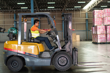 Asian male driver driving forklift to shipping delivery product in the warehouse distribution. import export logistic career, worker working at industrial factory.