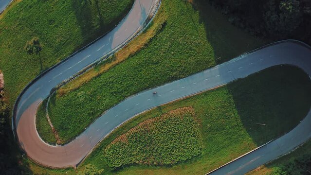 Top down view of pro woman cyclist riding at beautiful sunset/sunrise surrounded by nature on a curvy, winding S-shaped road. Cycling concept. Working out in the summertime. Being fit and healthy.