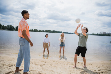 young man passing ball while playing beach volleyball with interracial friends.