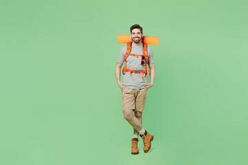 Full body fun smiling young traveler white man carry backpack stuff mat walk look camera isolated on plain green background Tourist leads active healthy lifestyle Hiking trek rest travel trip concept