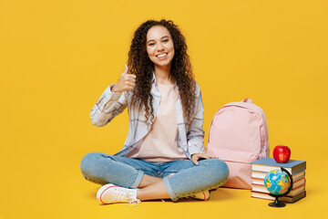 Fototapeta Full body young black teen girl student she wear casual clothes backpack bag sitting on floor near books show thumb up isolated on plain yellow color background High school university college concept. obraz