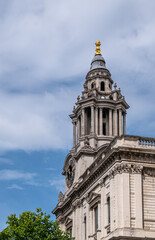 Fototapeta na wymiar London, England, UK - July 6, 2022: St. Paul's Cathedral. Gray stone SW clock tower at front entrance against blue cloudscape. Golden ornament on top. Baroque style with pillars. 