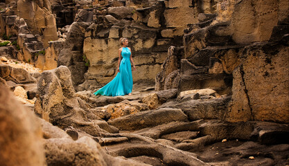 Beautiful slim blonde woman in turquoise blue long dress walks among strange rocks in the middle of...