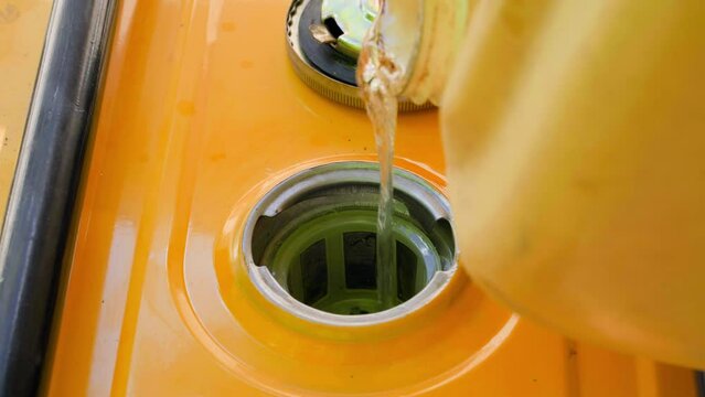 Fuel is poured into the fuel tank of a yellow gas generator from a plastic canister close-up. Refueling a gasoline generator. A jet of clear clean gasoline into the filler neck