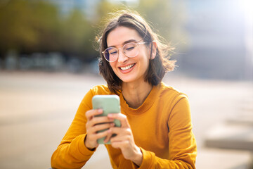 Smiling young woman sitting outside using her phone