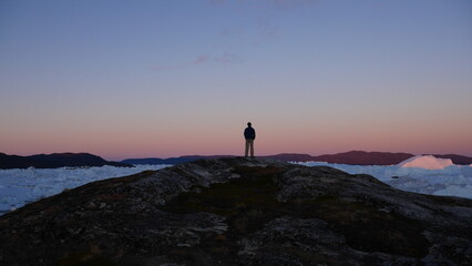 Person standing on cliff overlooking icebergs in Greenland