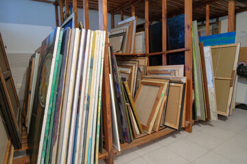 Fototapeta na wymiar Wooden shelves full of pictures, frames and art equipment. Art gallery storage