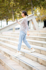 Young woman walking down the stairs outside and listening to music from phone