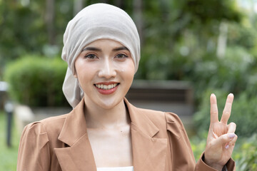 Hopeful rehabilitating Asian woman cancer patient showing V for victory, winning cancer and tumor...