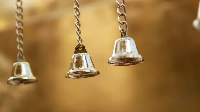 Small decorative gold metal bells hanging and swaying against gold background.