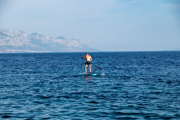 Man standing and rowing on his paddle board across the Mimice beach bay, Croatia