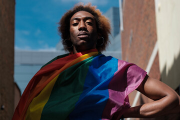 A very serious non-binary young person is holding a lgbtq flag in a street of London.
