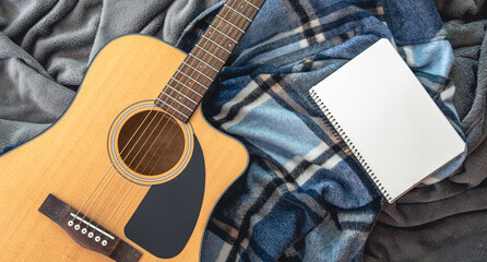 Acoustic guitar and notepad on a plaid background, top view.