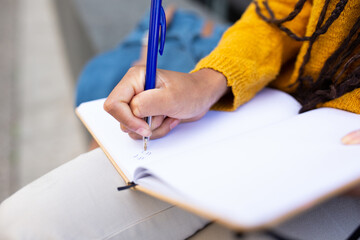 Girl writing with pen and book while sitting outside