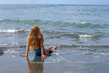 happy girl sits on the shore of the blue sea, horizontal