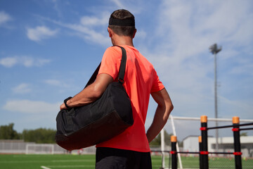 Back view of sportsman with bag standing at the open stadium