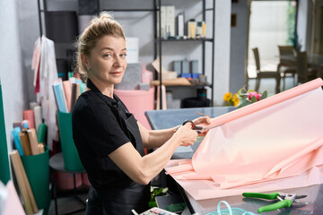 Woman florist cuts paper for bouquet and looks at camera