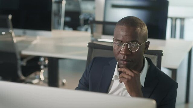 African-american attractive businessman in suit working on laptop in office, happy black ceo looking at computer screen thinks and analyzes looking at the computer screen, browsing web, using software