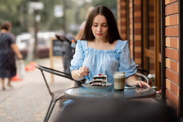 young woman is having coffee and cake outside by the street, lady eating dessert on outdoors cafe
