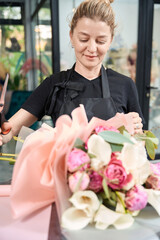 Joyful female florist holding scissors and looking at finished bouquet