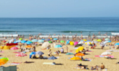 Blurred photo of ocean beach full of tourists under sun umbrellas in the summer day. Vacation background.
