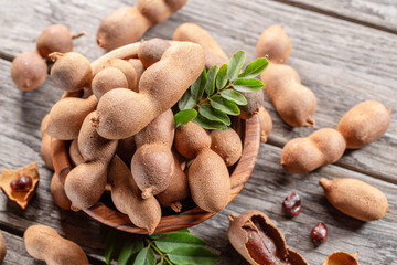 Ripe tamarind fruit, leaves and some tamarind seeds on wooden table.
